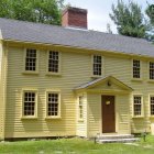 Yellow two-story house with gabled roof and white trim, front porch, surrounded by green trees.