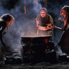 Women performing mystical ritual around cauldron in dimly lit setting