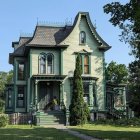 Victorian-style house with blue exterior, white trim, front porch, lush greenery under partly cloudy