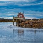 Vivid red boathouse on rocky pier by calm waters with red boat.