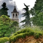 Lush garden with blooming orange flowers, tall trees, grand tower, and bird in flight.