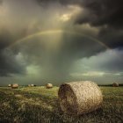 Vibrant rainbow over golden hay bales in scenic field