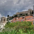 Lush garden painting with blooming flowers and classic buildings under dramatic sky