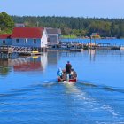 Tranquil waterfront with white building, boats, and colorful sailboat on sunny day