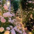 Tranquil garden pathway with pink and white roses, white columns, lanterns, and lush green