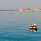 Vibrant painting of boats on calm sea with cityscape under cloudy sky