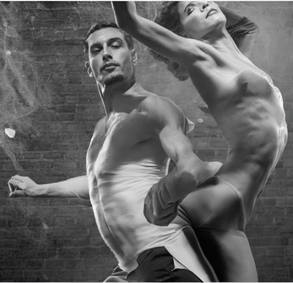 Shirtless man and woman dancers in dynamic pose with gritty backdrop