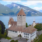 Scenic painting of lakeside monastery with clock tower, lush forests, and mountain backdrop