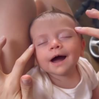 Baby with big smile gets nose touched by adult hand with brush