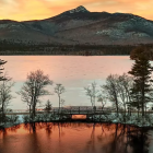 Tranquil sunset landscape with silhouetted trees, mountains, calm water, and dock