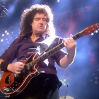 Musician in patterned shirt plays electric guitar on stage with colorful lights and floral backdrop