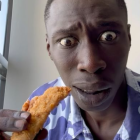 Digital portrait of person with glistening skin and water droplets, holding fried chicken, wearing blue jacket