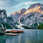 Tranquil lake scene with red boats, dock, lush trees, cliffs at dusk