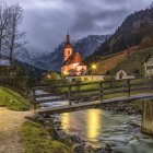 Snow-covered village with illuminated houses, church, river, and mountains under starry sky