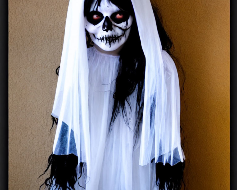 Ghost costume with skull face paint and red eyes against orange wall