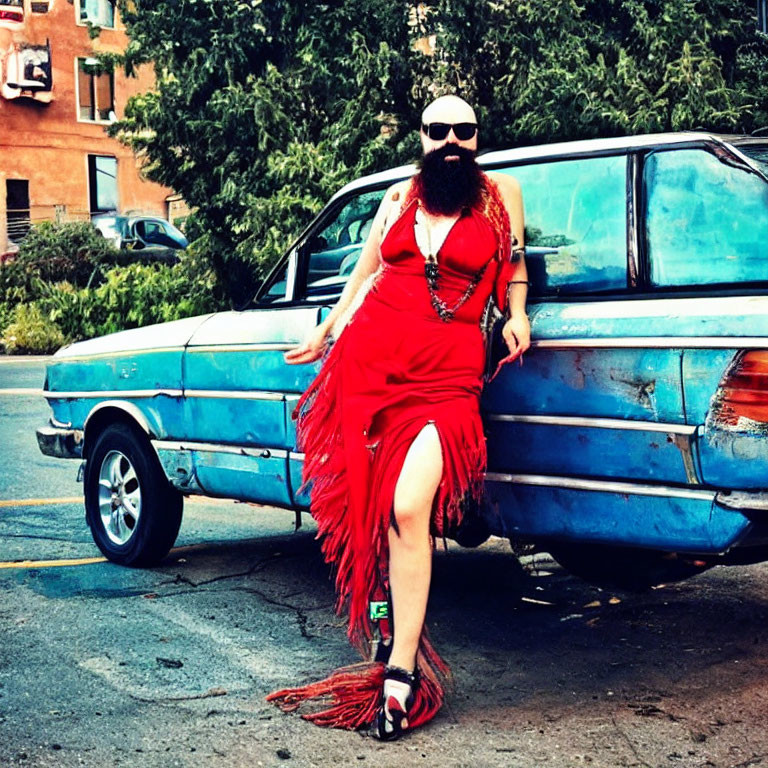 Bearded person in sunglasses leaning on blue car in red dress