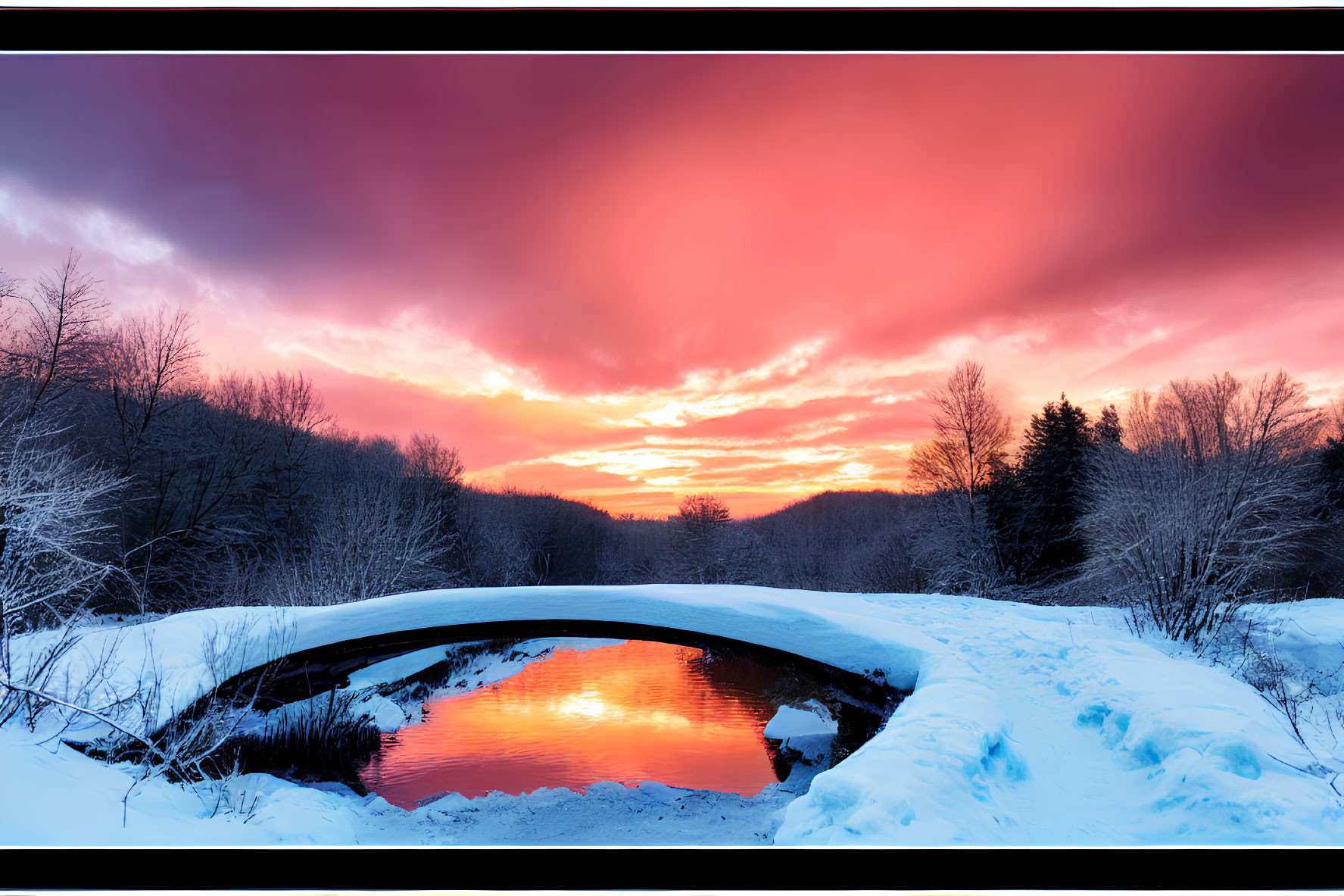 Fiery sunset reflecting on snow-covered river and bridge