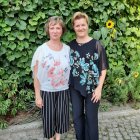 Women in flowing floral garments amidst lush greenery and vibrant flowers