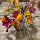 Vibrant still-life painting of flowers, fruit, and ornaments on reflective surface