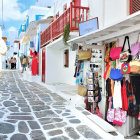 Scenic narrow street with white-washed buildings, vibrant flowers, cobblestone pavement, and blue