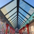 Glass-covered walkway with red pillars leading to building with people underneath