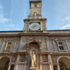 Historic clock tower with statue against cloudy sky.