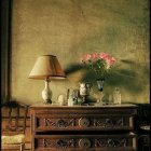 Vintage wooden cabinet with books and pottery under a classic lamp in cozy interior scene