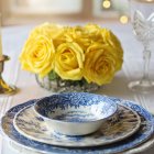 Sophisticated table setting with gold accents, blue china, yellow flowers, candles, and crystal glass