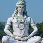 Blue-skinned Lord Shiva statue with gold jewelry, sitting calmly under clear sky