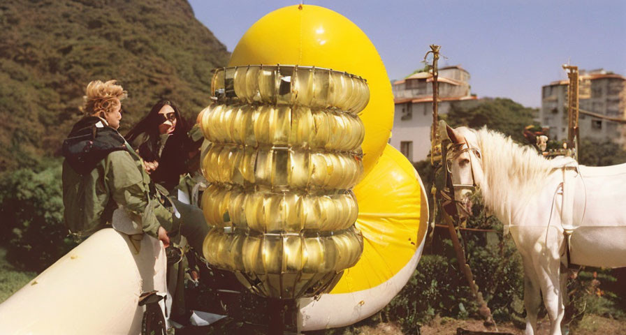 Two people with yellow and silver sculpture, white horse, green hills.