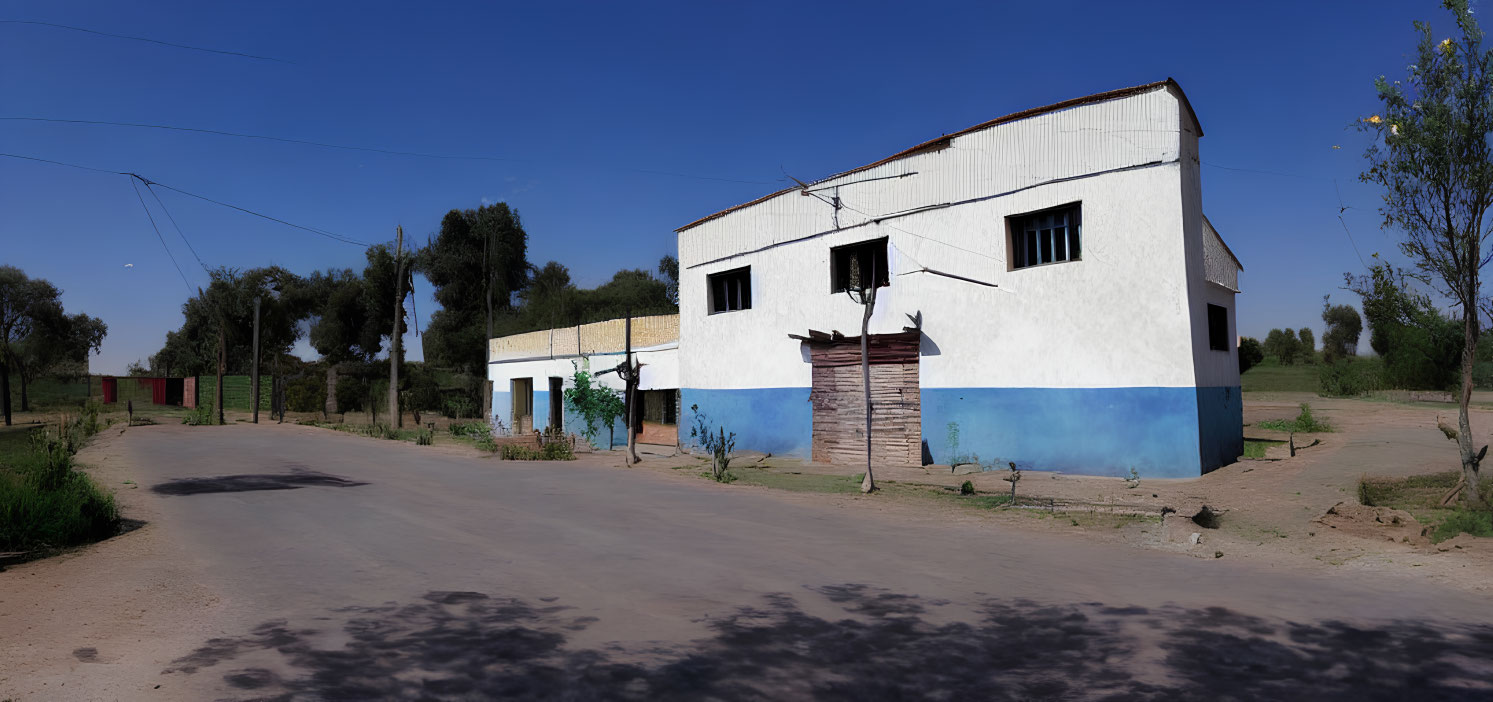 Deserted rural road with white & blue building under clear sky