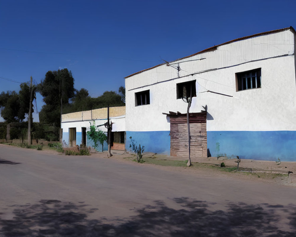 Deserted rural road with white & blue building under clear sky