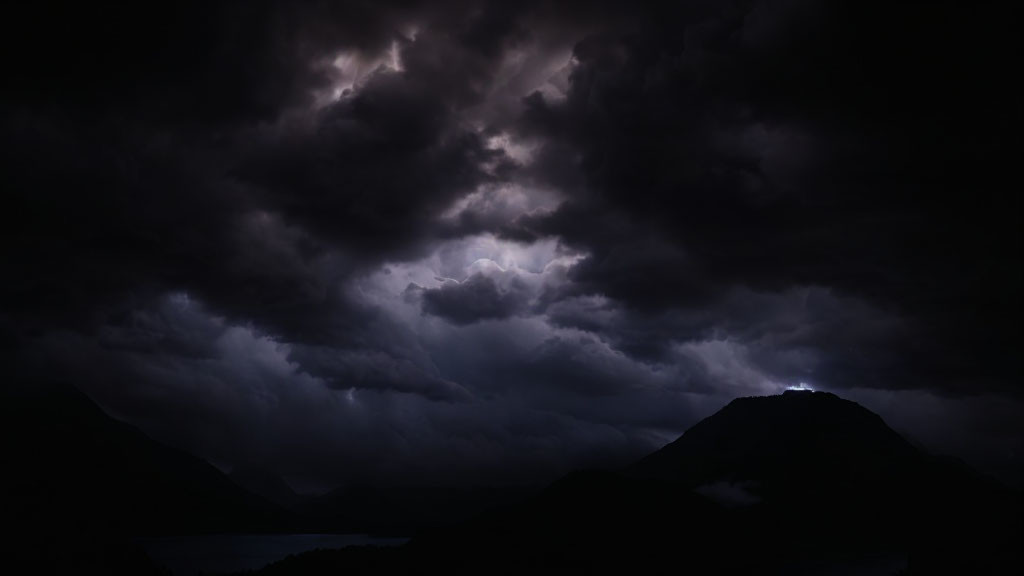 Dramatic night scene: mountains, dark clouds, subtle lightning