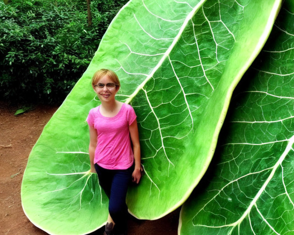 Smiling person with glasses next to oversized leaf in green environment