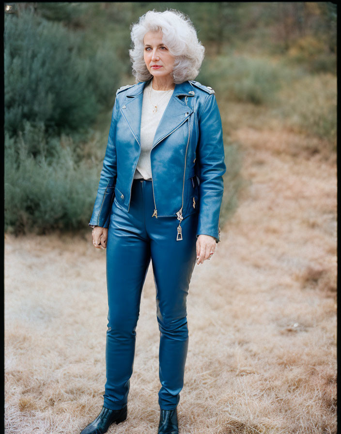 Curly Gray-Haired Woman in Blue Leather Outfit in Dry Grass Field