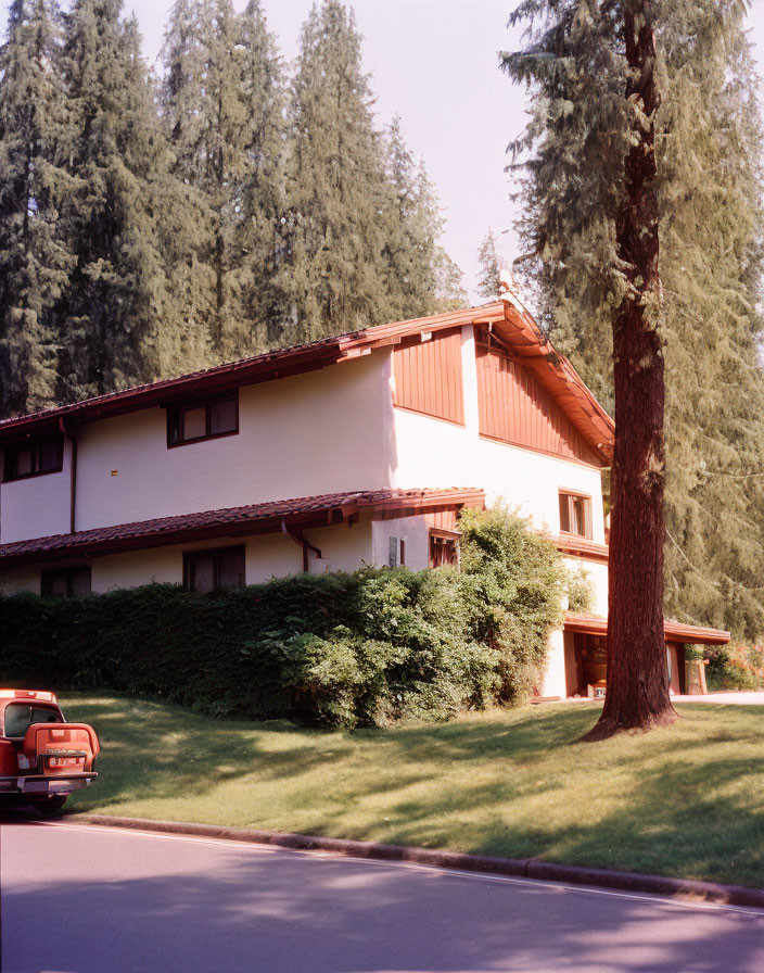 White-walled two-story house with red roof, vintage car, and tall trees