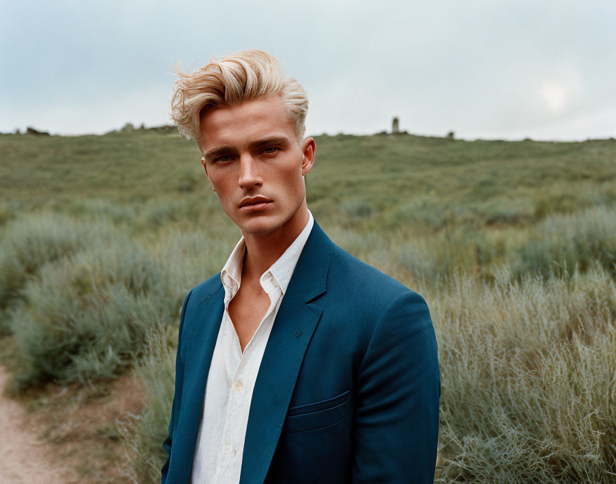 Blond man in navy blazer outdoors with grassy field