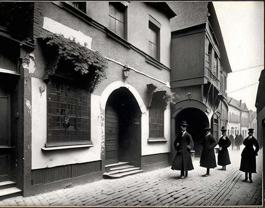 Vintage black and white photo of people in early 20th-century clothing on cobblestone street