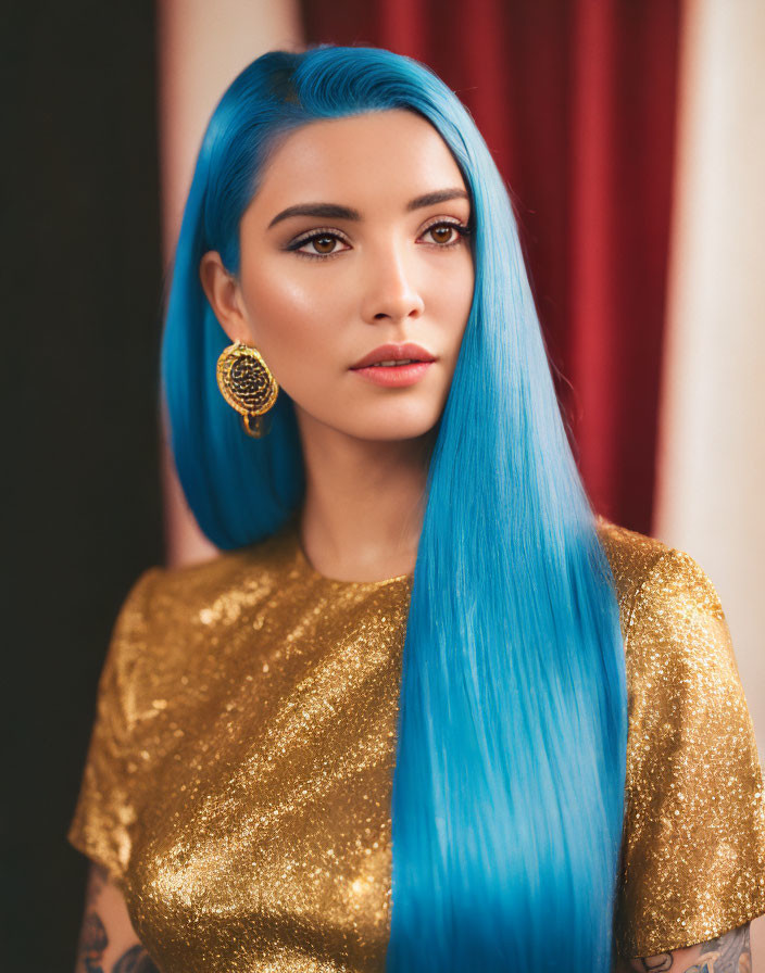 Vibrant blue-haired woman in golden top with detailed earring and arm tattoo.