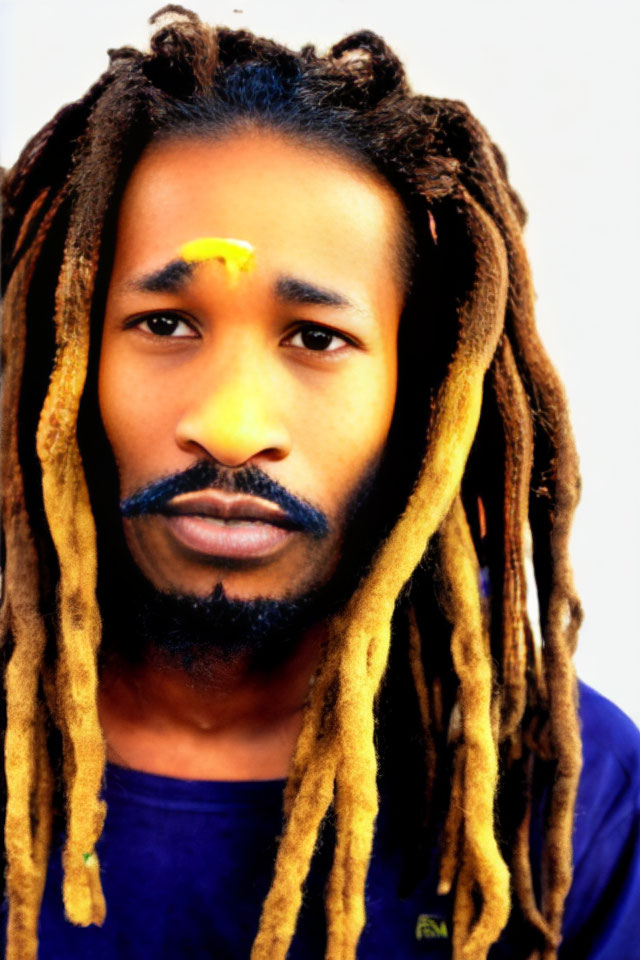 Pensive man with dreadlocks and painted forehead gazes at camera