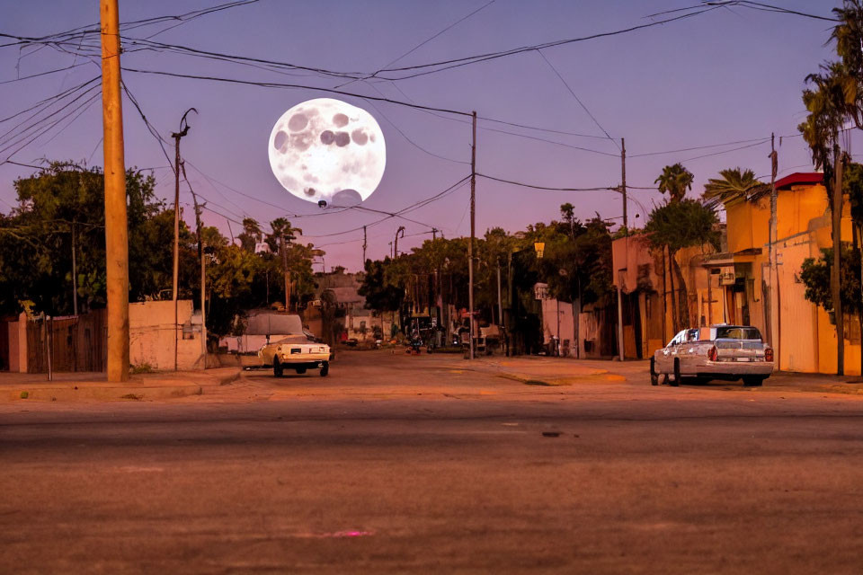 Deserted Street at Dusk with Oversized Moon, Parked Cars, Houses, and Palm