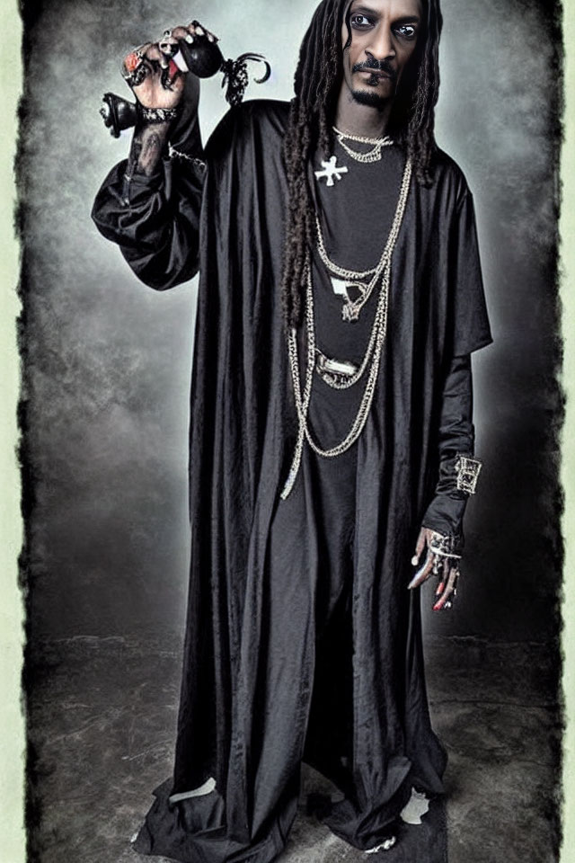 Person with long black dreadlocks in black robe rings bell in front of dark backdrop