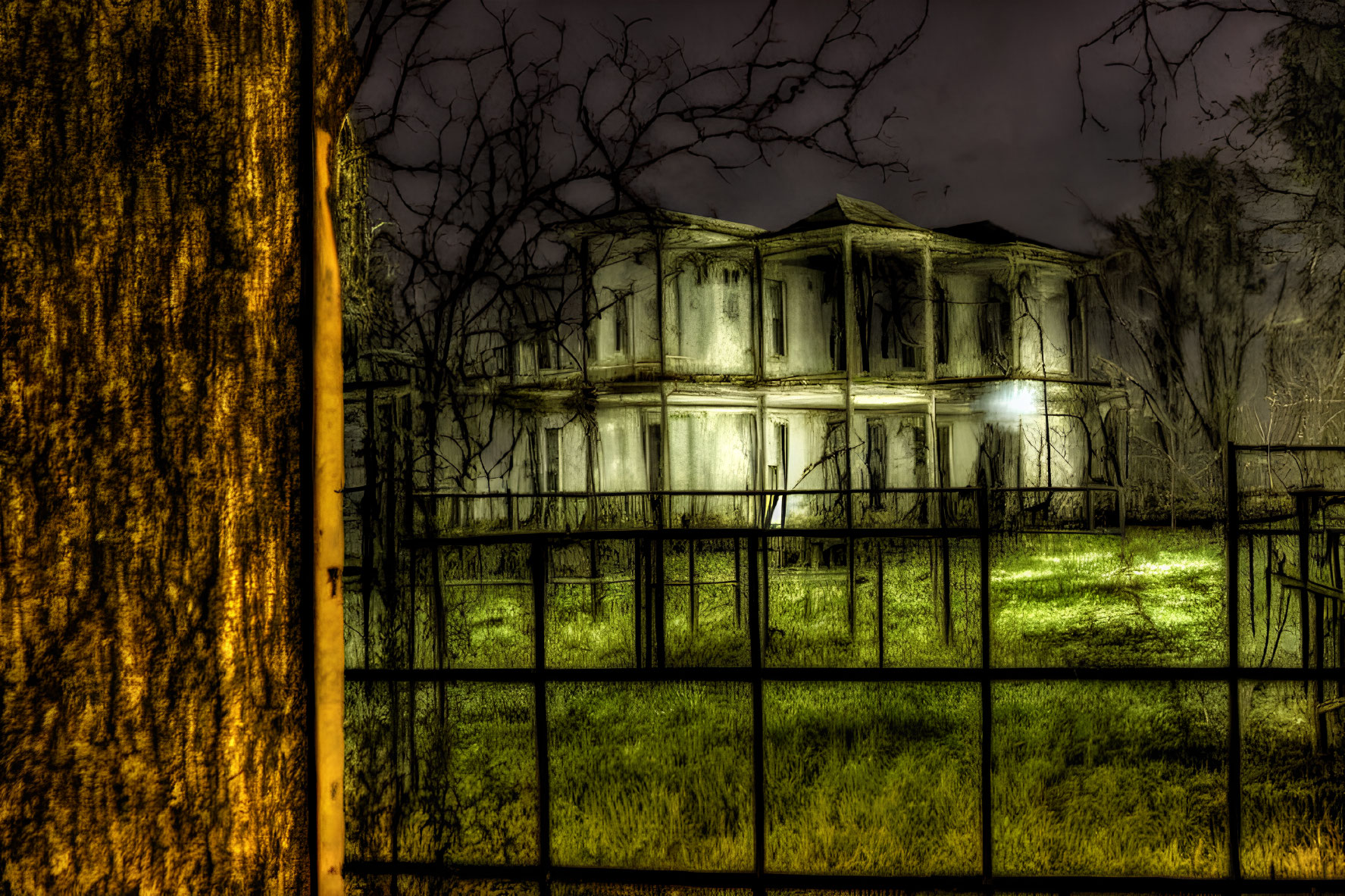 Abandoned two-story house at night with eerie lighting and metal fence