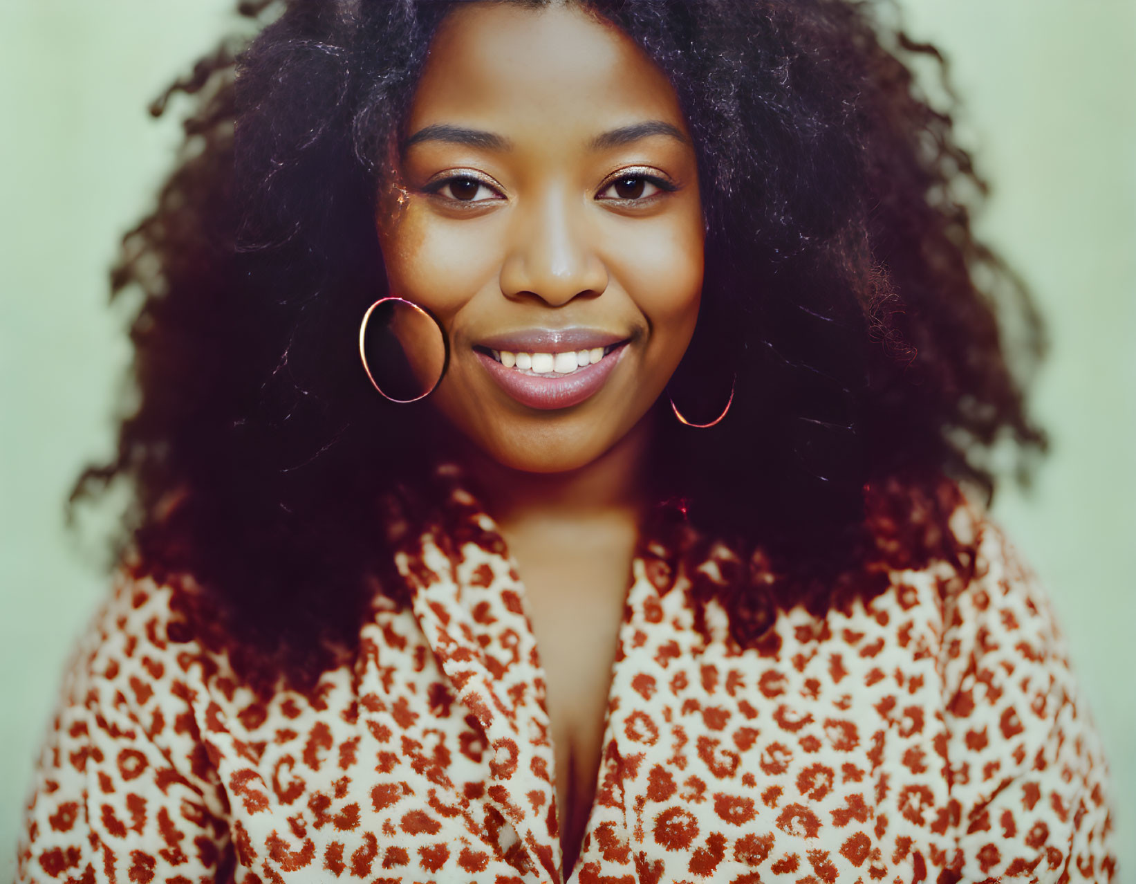 Smiling woman with curly hair in leopard print top on green background