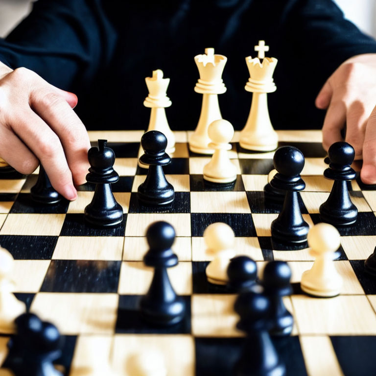 Person in black shirt playing chess with hand on black pawn, white pieces in background