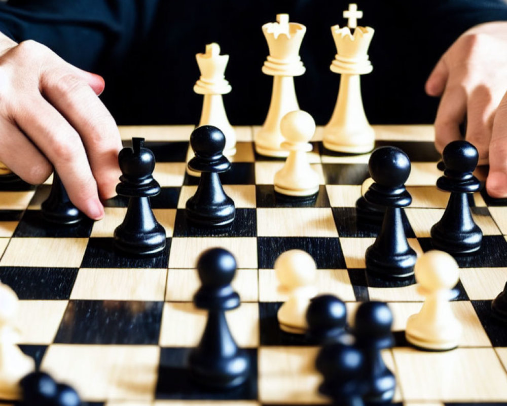 Person in black shirt playing chess with hand on black pawn, white pieces in background