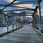 Colorful painting: old steel bridge over river to cityscape at sunset