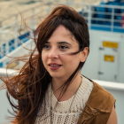 Smiling woman with brown hair in white top and jacket, blurred background.