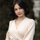 Dark-haired woman in white attire with silver earrings on dappled light background