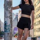 Urban setting with woman in black crop top and skirt posing near graffiti-covered pillar.